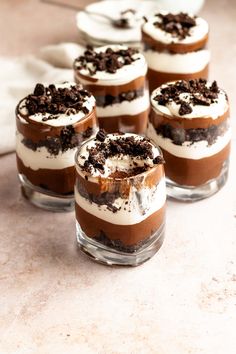 four desserts in small glass dishes with chocolate and cream toppings on top, sitting on a table