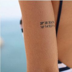 a close up of a person with a tattoo on her arm and the ocean in the background