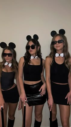 three women dressed up in mickey mouse ears and black outfits, one holding an umbrella