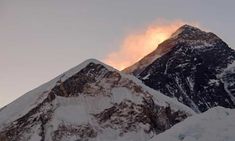 the top of a mountain covered in snow with clouds coming out of it's summit