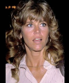 a woman with blonde hair and blue eyes looks at the camera while wearing a white shirt