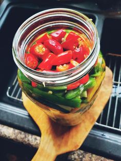 a jar filled with peppers sitting on top of a wooden cutting board