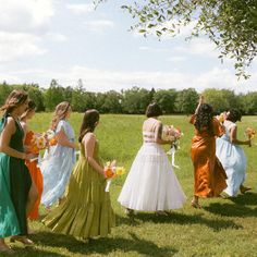 a group of women in long dresses standing on top of a grass covered field next to each other