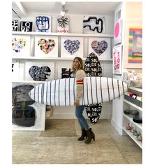 a woman holding a surfboard in a room with lots of art on the walls