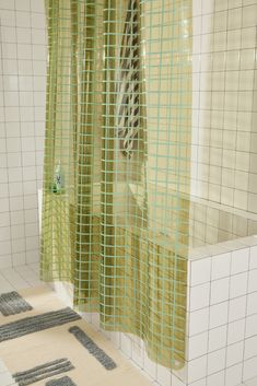 a bathroom with green and white tiles on the floor, shower curtain and rugs