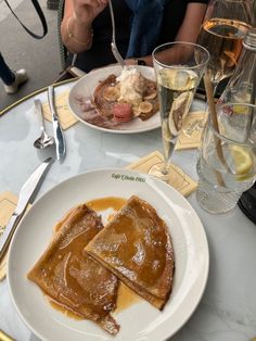 two plates of food on a table with silverware and wine glasses next to them