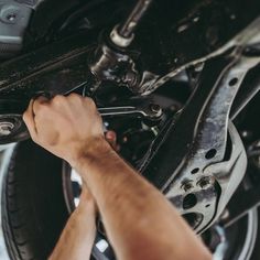 a man working on the underside of a car's front wheel and brake assembly