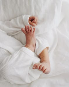 a baby laying on top of a bed covered in white blankets and holding the end of his leg