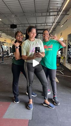 three women taking a selfie in the gym with their cell phones and smiling at the camera