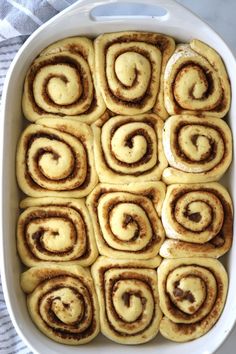 cinnamon rolls in a white baking dish on a towel