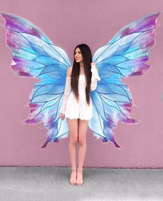 a woman standing in front of a pink wall with a blue butterfly wings on it