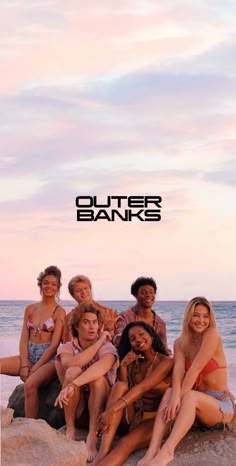 a group of young people sitting on top of a beach next to the ocean in bathing suits