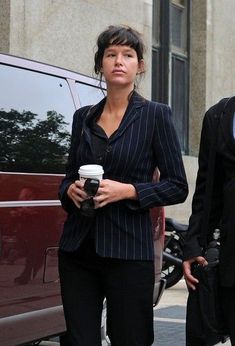 a man and woman walking down the street while holding coffee in their hands, with a red van behind them