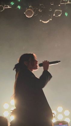 a man standing on top of a stage with a microphone in his hand and lights behind him