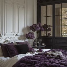 a bed with purple and white comforters in a bedroom next to a large window