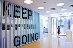 a woman is standing in front of a wall with posters on it that say keep going