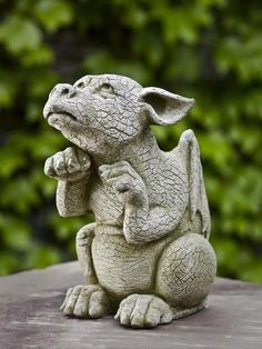 a small statue of a dragon sitting on top of a wooden table in front of some bushes