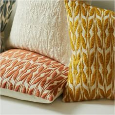 three pillows sitting next to each other on top of a white table with an orange and yellow pattern