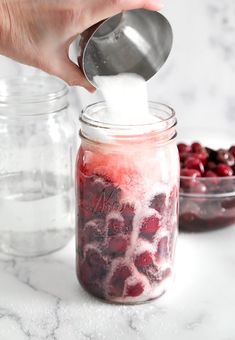 someone pouring sugar into a jar filled with cranberries