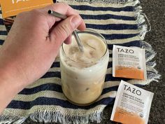 a person holding a straw in their hand next to some tazo packets and a drink