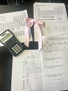 a calculator sitting on top of papers with pink ribbon tied around the ends