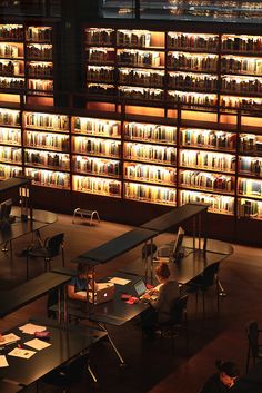 people are sitting at tables in front of bookshelves with lights on the shelves