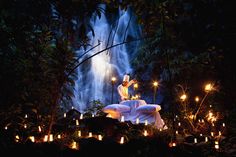 the statue is surrounded by candles and lights in front of a waterfall with water cascading