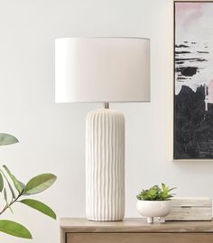 a white lamp sitting on top of a wooden table next to a potted plant