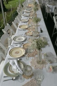 a long table is set up with plates and silverware for an outdoor dinner party