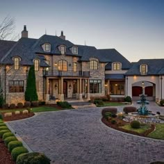 a large house with a fountain in the front yard and landscaping around it at dusk