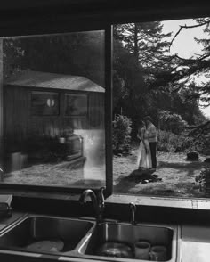 black and white photograph of two people standing in front of a kitchen window with an old photo on it