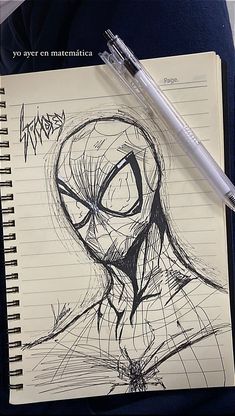 a pen is sitting on top of a notebook with a drawing of a spider man