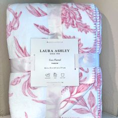 a pink and white floral print blanket with label on it's side, in front of a wall