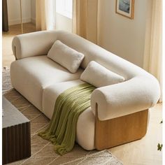 a white couch sitting on top of a wooden floor next to a window with curtains