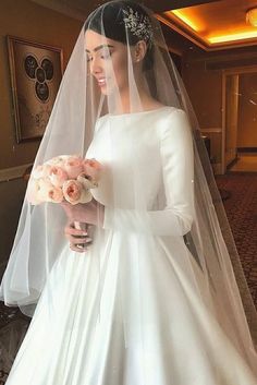 a woman in a white wedding dress holding a bouquet of flowers and wearing a veil