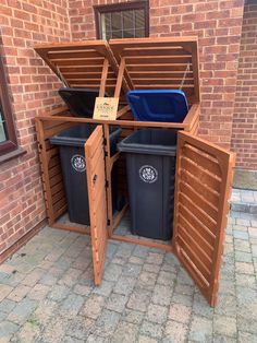 two trash cans are in the middle of an open wooden box on the side of a brick building