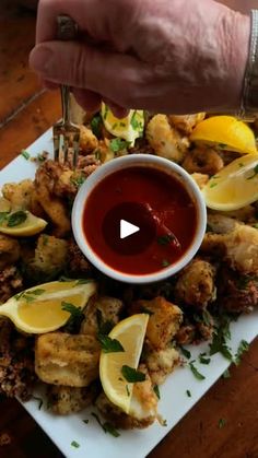 a person is dipping sauce on top of some fried food with lemons and parsley