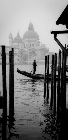 a person on a boat in the water near some poles and piers with buildings in the background