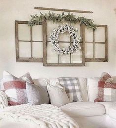 a living room with white couches, pillows and wreaths hanging on the wall