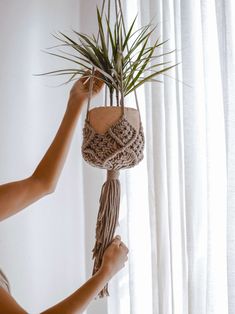 a woman holding up a plant hanging from a rope