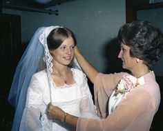 two women dressed in wedding attire, one is fixing the bride's veil