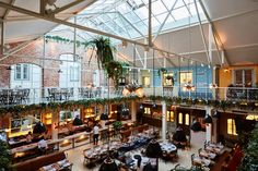 the inside of a restaurant with tables and chairs, plants on the wall, and high ceilings