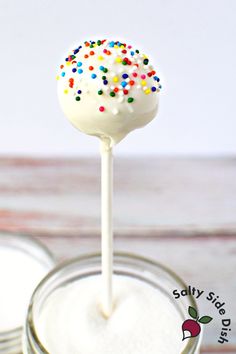 a white cake pops with sprinkles on top sitting in a glass jar