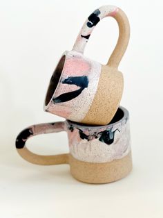 two coffee mugs sitting next to each other on a white surface with black and pink designs