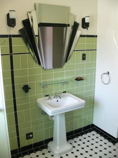 a white pedestal sink sitting under a mirror in a bathroom next to a green tiled wall