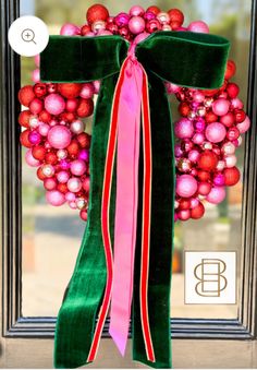 a green wreath with pink and red ornaments hanging on it's front door window