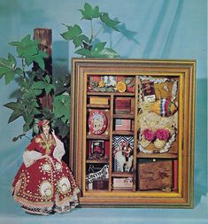 a doll is standing next to a wooden box with many items in it and a potted plant