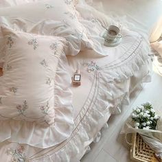 a white bed topped with lots of pillows next to a basket filled with flowers on top of it