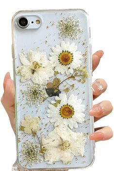 a woman's hand holding an iphone case with white flowers on the front and gold flakes on the back