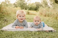 two toddlers laying on a blanket in the grass